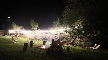 Un espacio al aire libre con asientos nocturnos, una chimenea, sillas y luces colgantes.