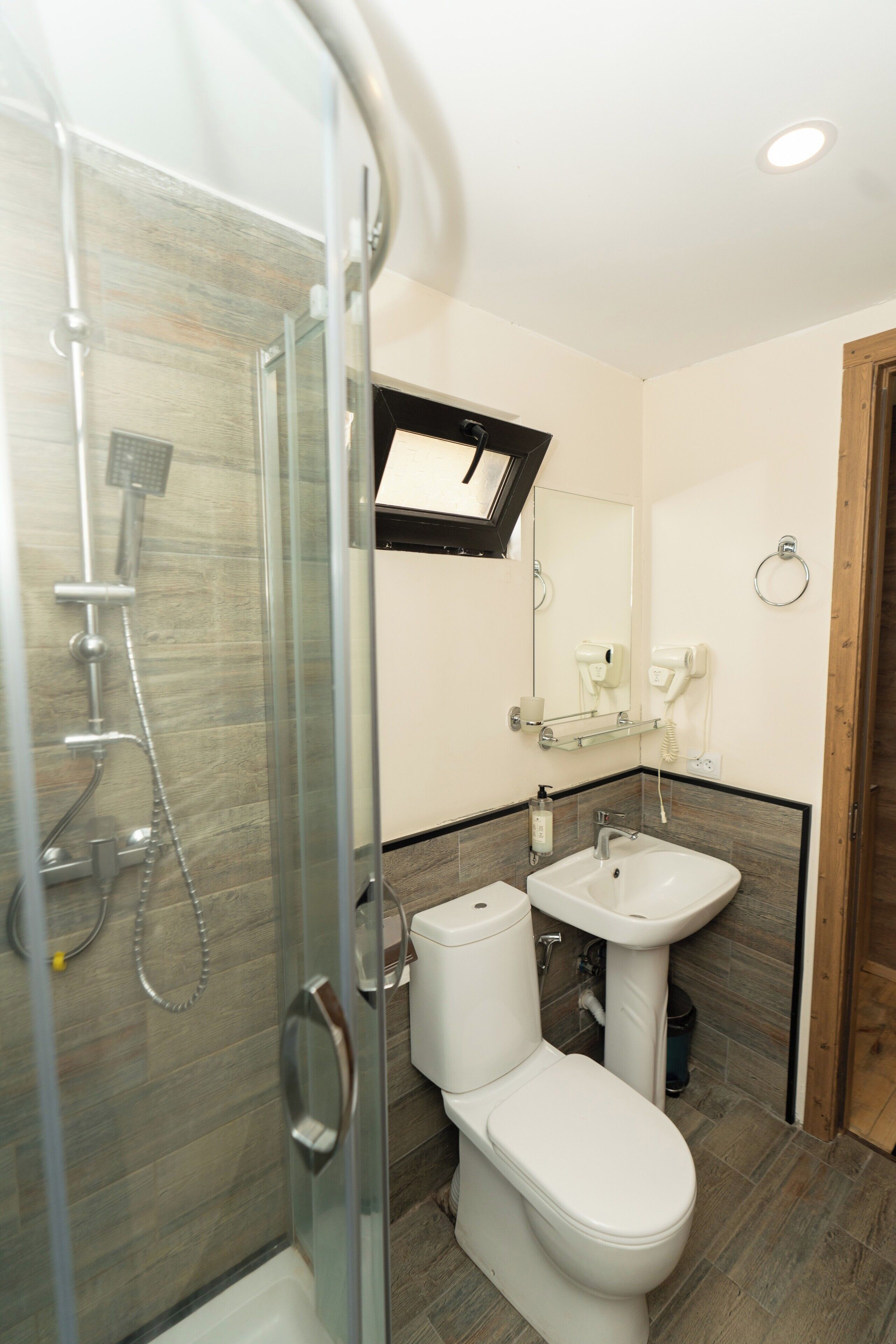 A modern bathroom with a glass shower enclosure, a white toilet, and a sink with a mirror above.