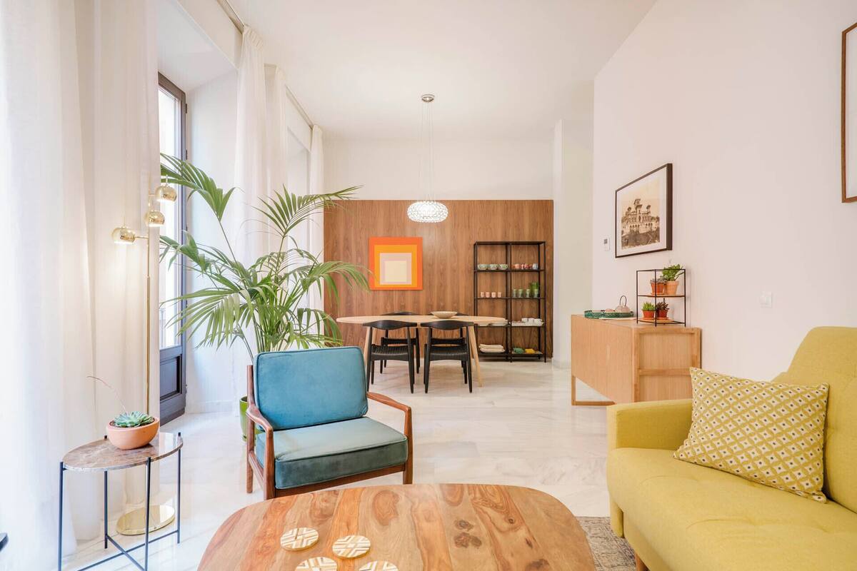A modern living room with a sofa, a coffee table, a dining area with a table and chairs, and a bookshelf.