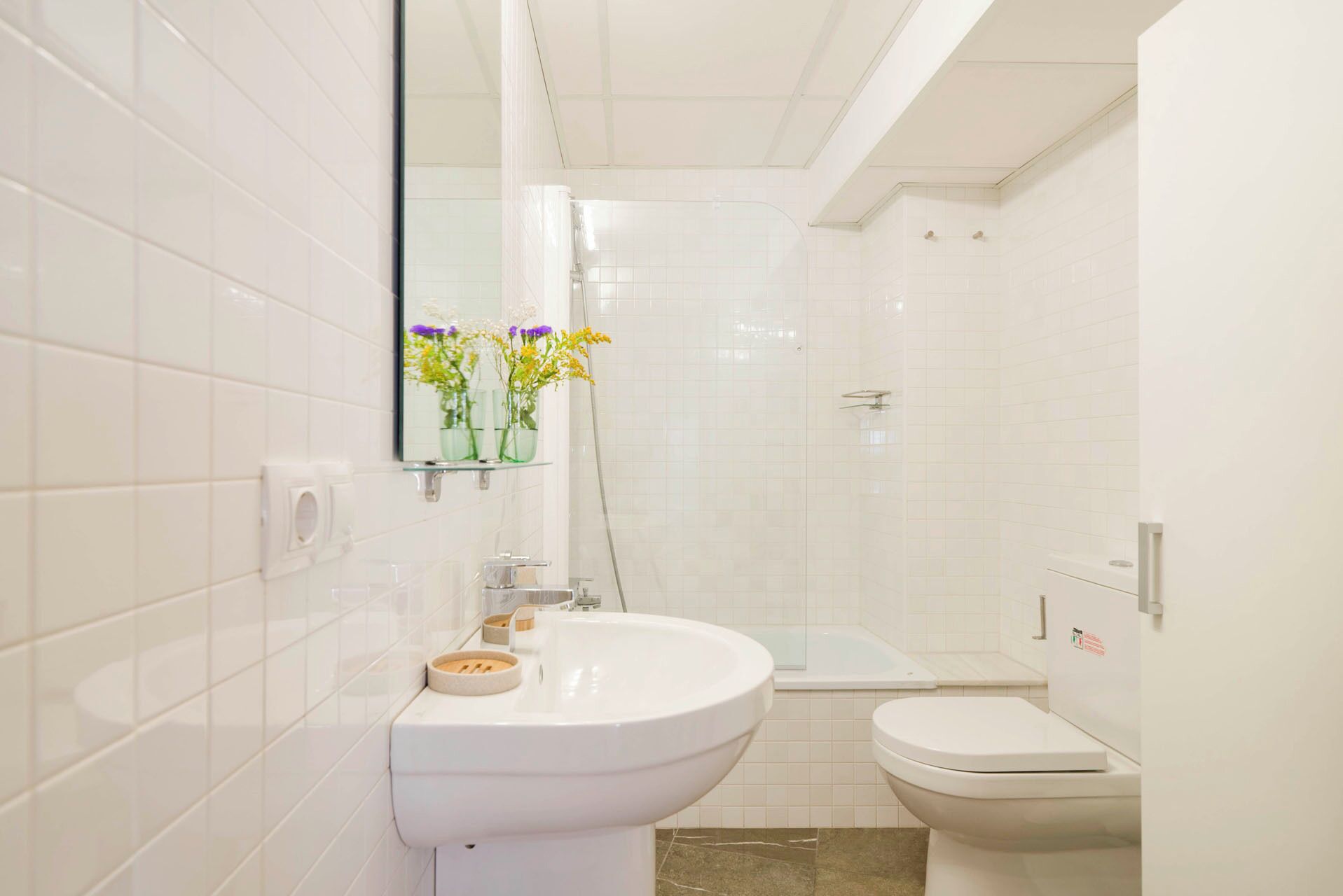 Ein Badezimmer mit weißen Fliesen, einem Waschbecken, einer Toilette und einer Duschkabine.
