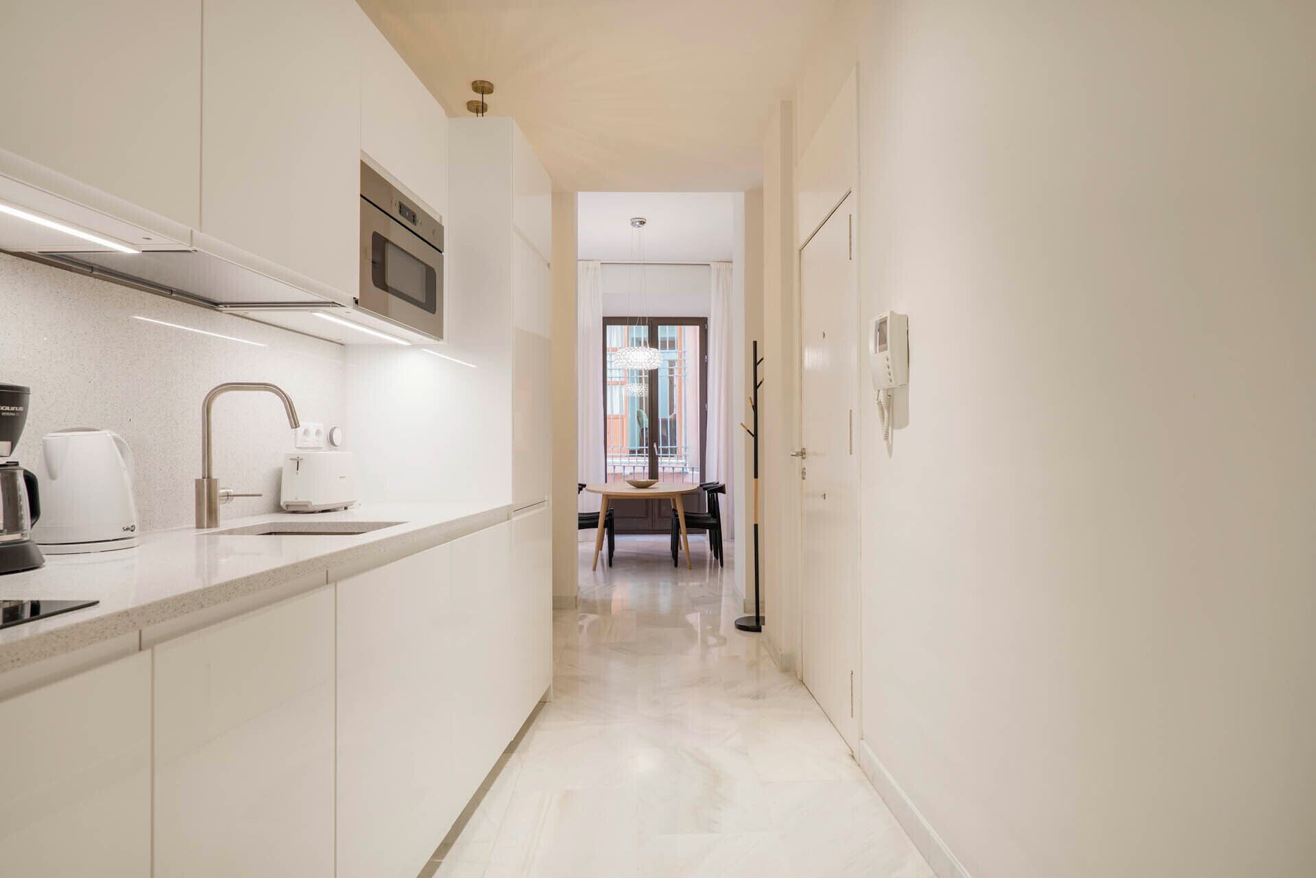 A modern kitchen with white cabinetry, a built-in oven, and a coffee machine.