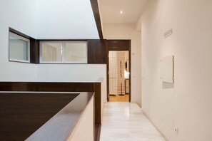 A modern interior with a wooden reception desk, a hallway leading to a room with a sliding door, and a sign indicating a second floor. - Solaga - Larios Suites (Málaga)