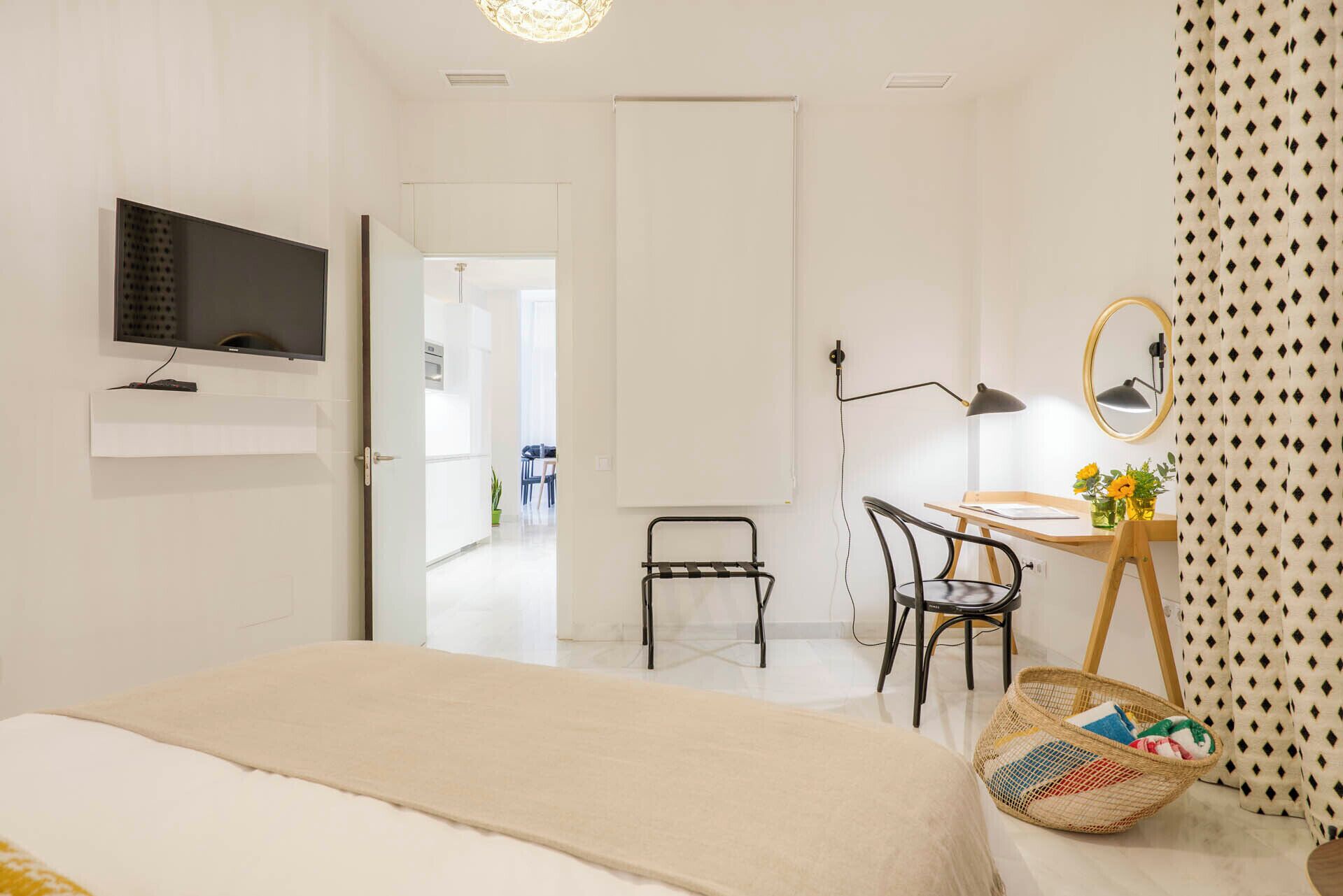 A modern bedroom with a bed, a desk with a chair, a TV mounted on the wall, and a mirror.