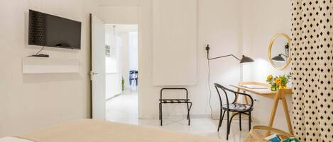 A modern bedroom with a bed, a desk with a chair, a TV mounted on the wall, and a mirror.