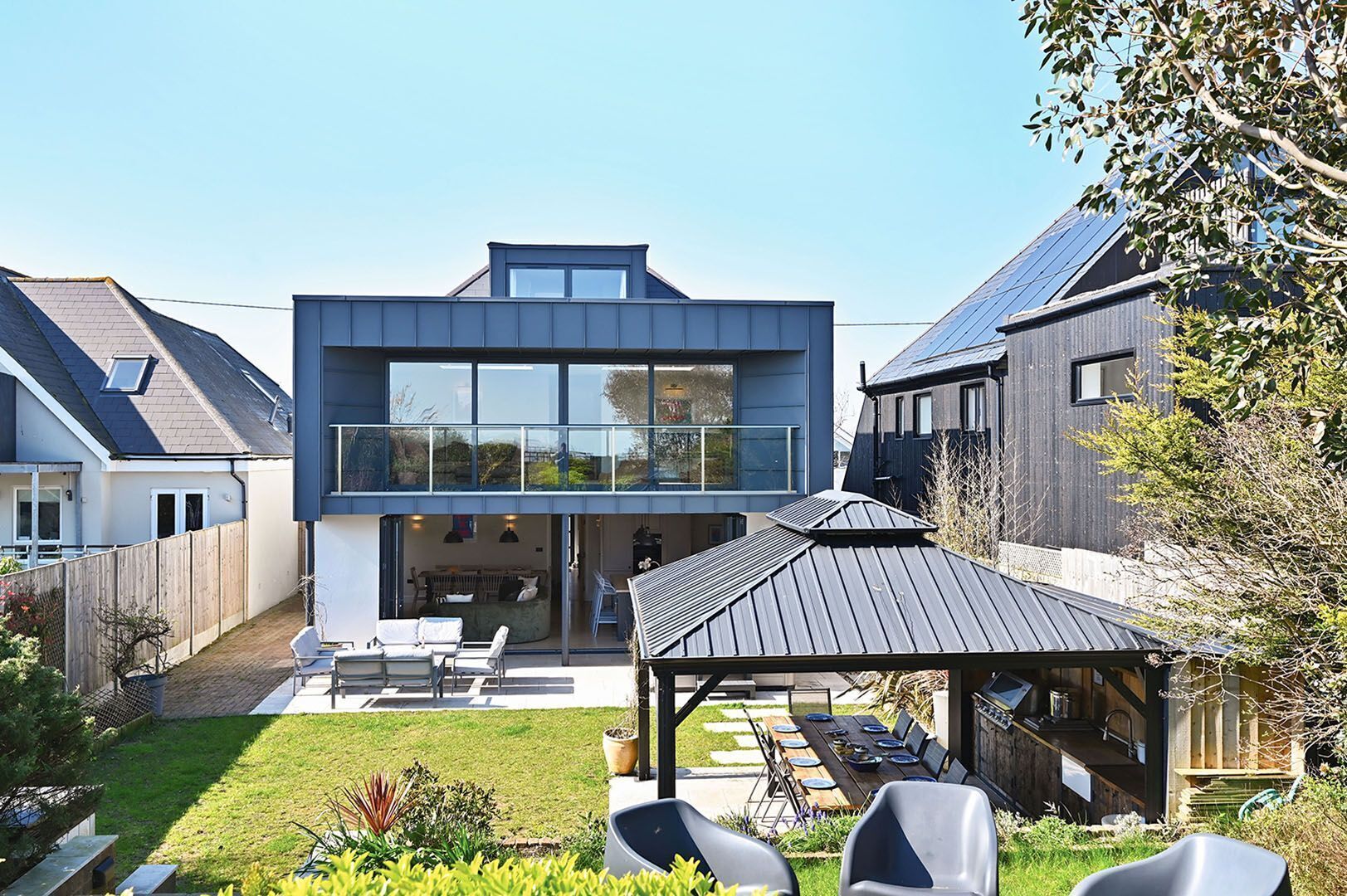 A modern two-story house with a patio, a covered outdoor seating area, and a visible garden.
