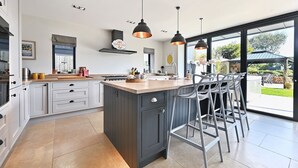 Cocina moderna con una isla central, taburetes de bar, iluminación colgante y vistas al exterior.