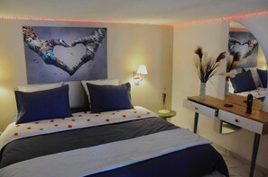 Une chambre d’hôtel avec un lit, une table de chevet, un miroir et un mur orné d’une œuvre d’art en forme de cœur.