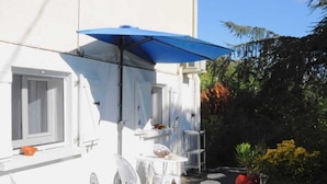 Een wit gebouw met terras, barbecue en blauwe parasol.