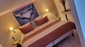 Een netjes opgemaakt bed met rozenblaadjes, twee bedlampjes, een wanddecoratie en een vaas met gedroogde planten.