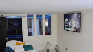 Een moderne woonkamer met een witte bank, een ronde houten salontafel en een aan de muur bevestigde televisie.