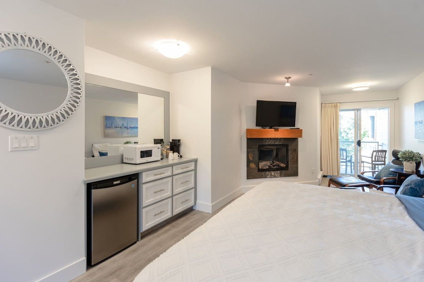 A hotel room with a bed, a fireplace, a television, a dining area with chairs, and a kitchen area with a microwave.