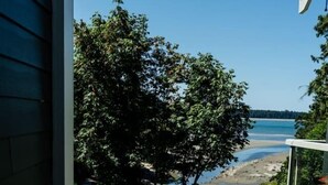 A view from a window overlooking a beach with trees and a clear sky. - Ocean Breeze Seaside Studio Condo B (Nanoose Bay)
