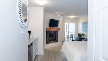 A hotel room with a fireplace, a television mounted on the wall, a bed with a white duvet, and a dining area with a table and chairs.