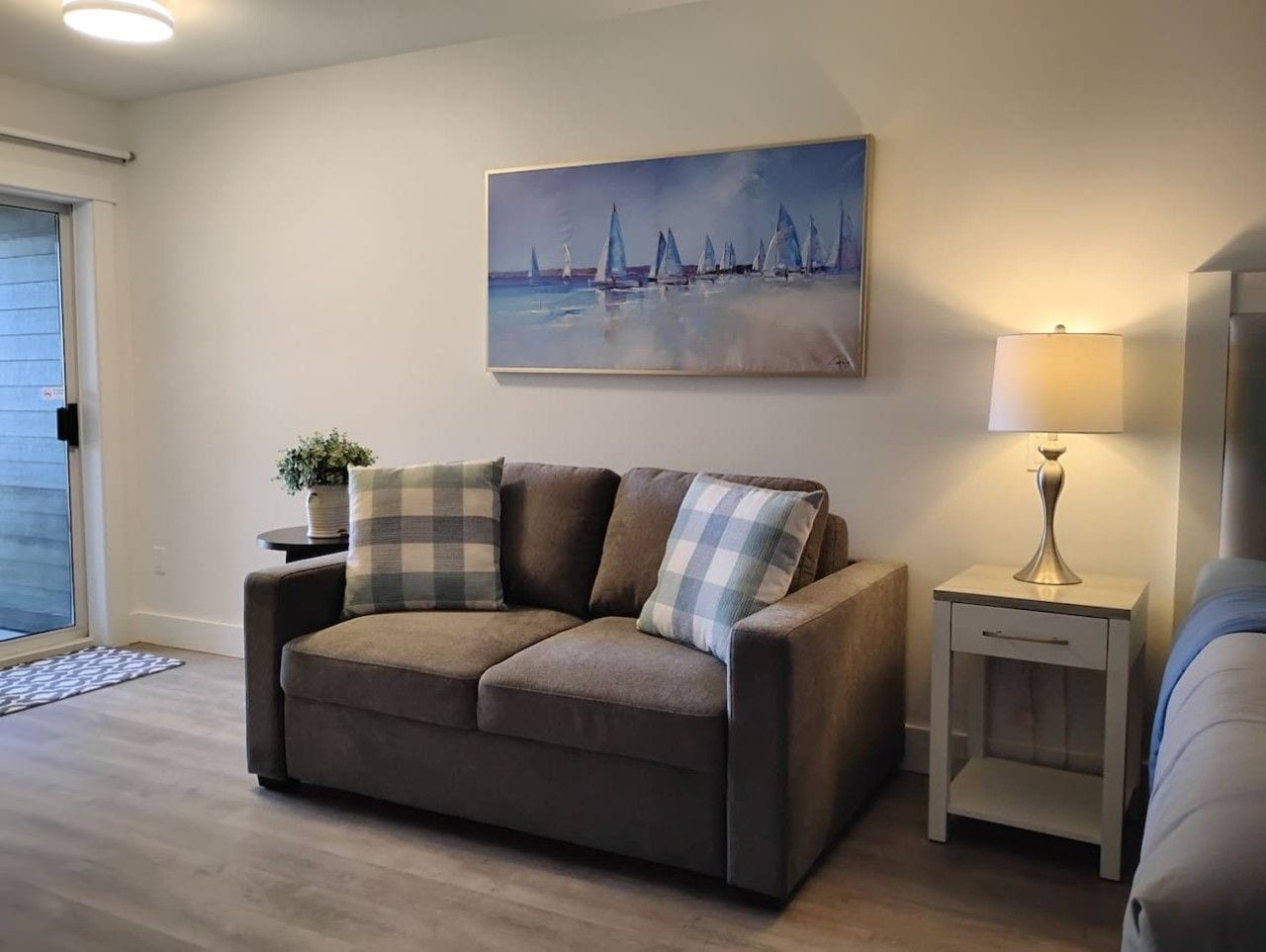 A living room with a sofa, a painting, a lamp, and a small table with a plant.