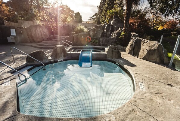Una piscina con suelo de azulejos, un tobogán azul y una escalera de metal.