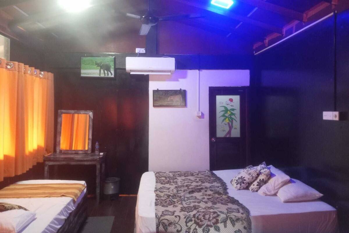 A room with two beds, a ceiling fan, an air conditioner, and a television on the wall.