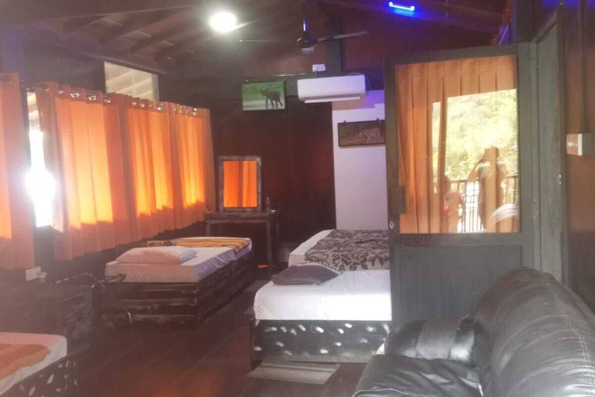 A room with two beds, a sofa, wooden floors, and a ceiling fan.