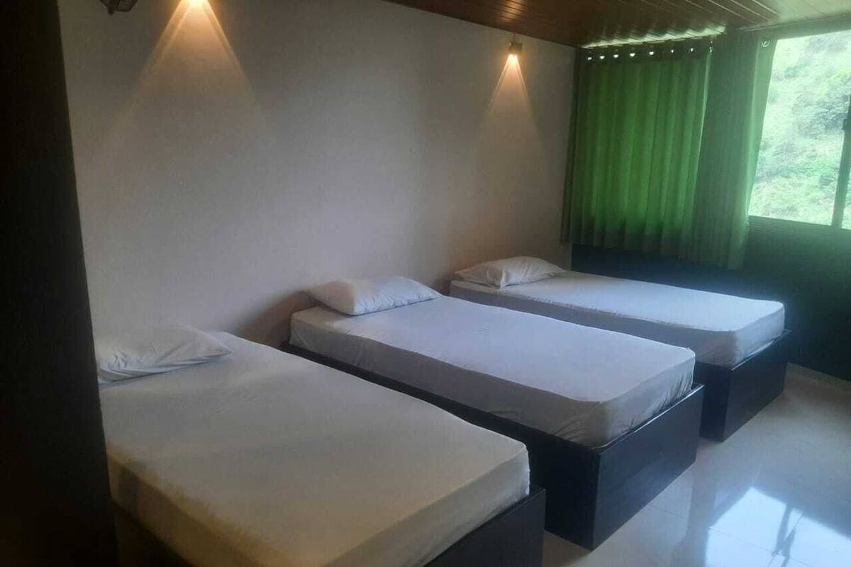 A room with three single beds, each with a pillow and a neatly folded blanket.