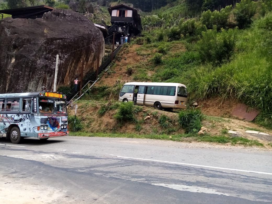 A bus on a road with a van parked on a hillside.