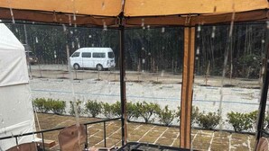 Un espace extérieur aménagé avec une table et des chaises, une tente au-dessus, et une vue sur un parking où se trouve un fourgon blanc.