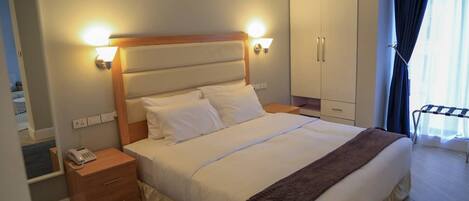 Une chambre d’hôtel avec un grand lit, des lampes de chevet, une table de chevet en bois, un téléphone, une armoire et une fenêtre avec des rideaux.