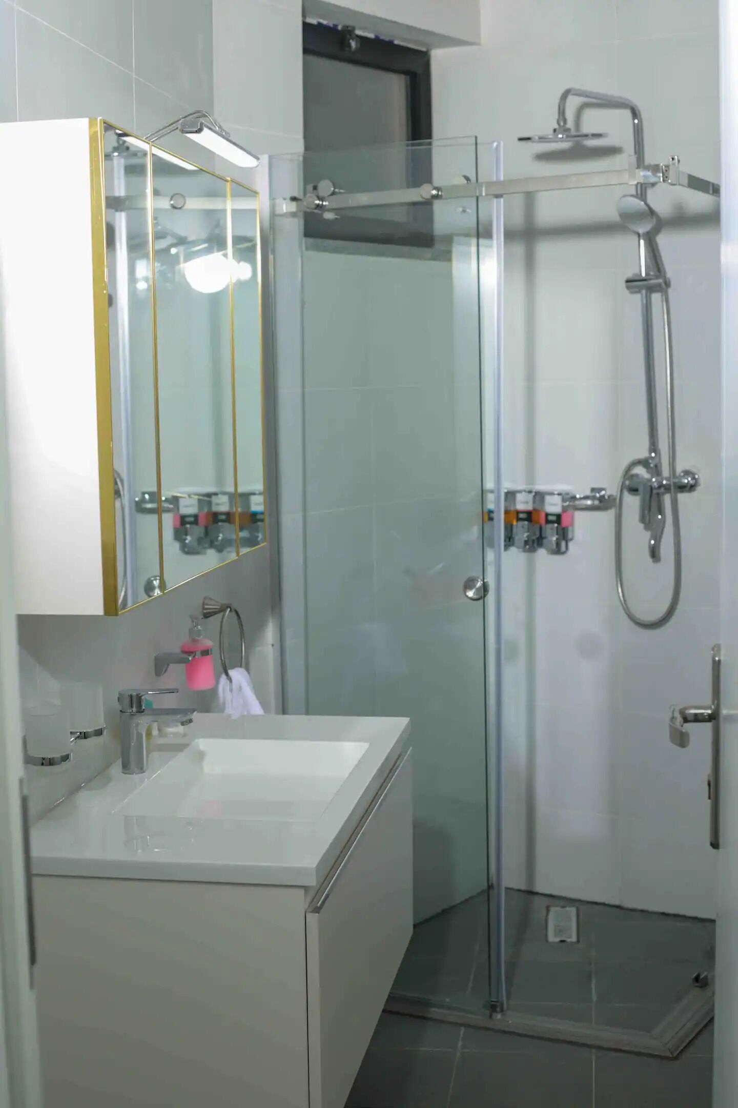 A modern bathroom with a glass-enclosed shower, a white sink, and a mirror with a gold frame.