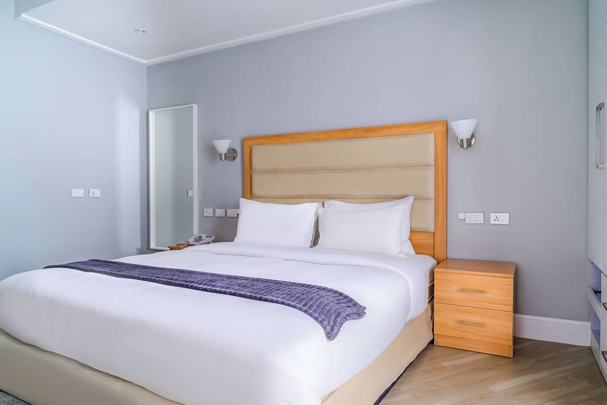 Une chambre d’hôtel moderne avec un grand lit, une table de chevet en bois et un miroir.