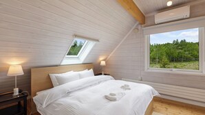 A bedroom with a sloped ceiling, a skylight, a large window, a bed with white linens, and a bedside lamp. - Gekko Hanazono (Kutchan)