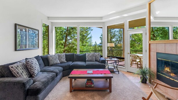A modern living room with a sectional sofa, a coffee table, and a fireplace. Large windows provide a view of the outdoors. - Snowcap Escape at Mount Bachelor w/ Pool & Hot Tub (Bend)