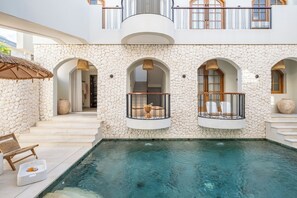A poolside area with a stone wall, arched windows, and a balcony with a railing. - LA LUNA (Canggu)