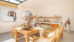 Een lichte keuken met een eethoek, met rieten meubels, een houten tafel en een grote vaas met gedroogde planten.