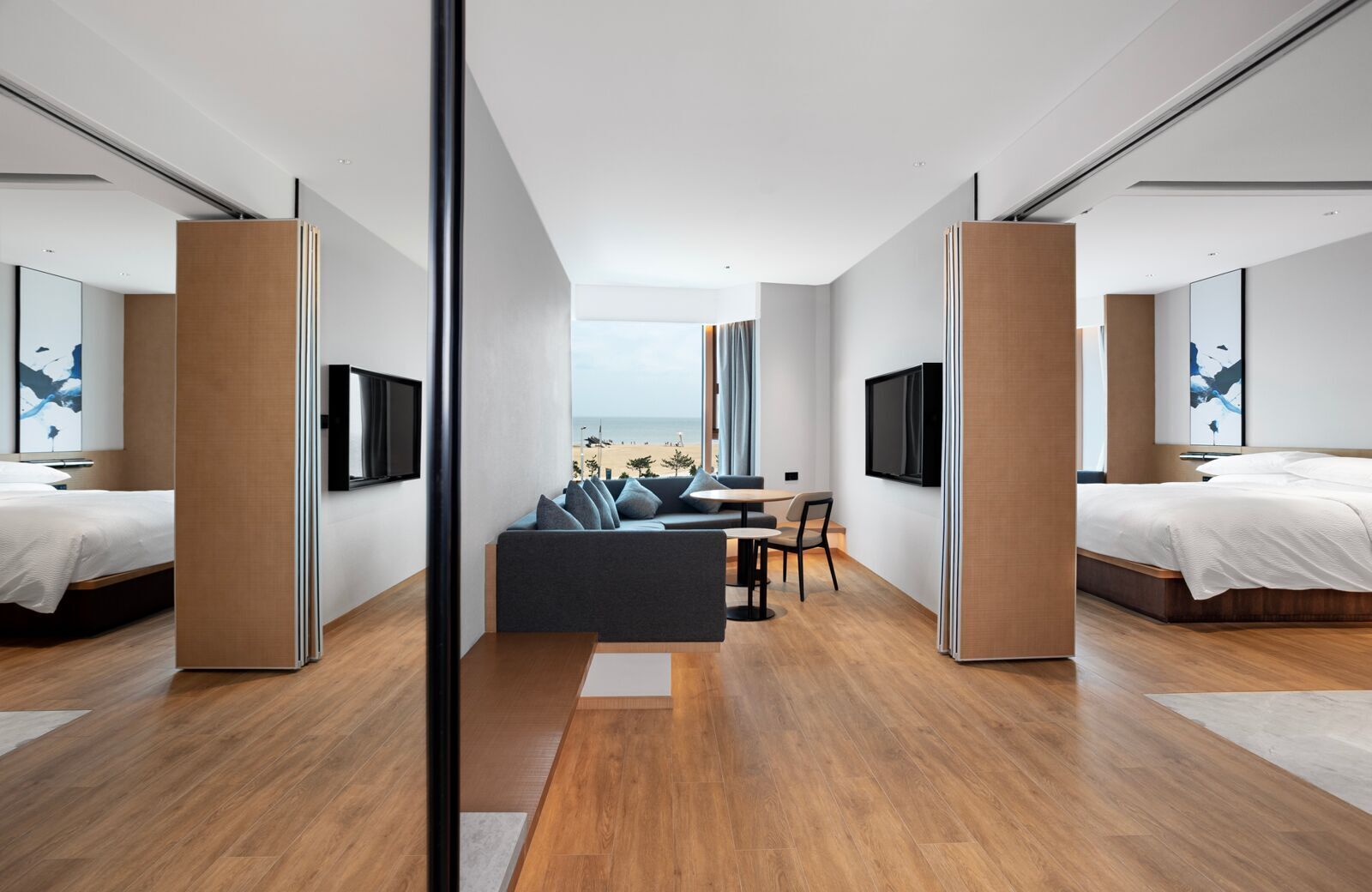 A modern hotel room with a sofa, a dining table, and two beds.