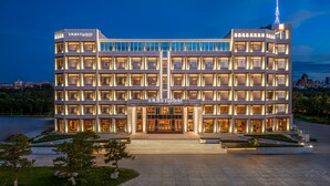 Un hotel moderno a più piani con una facciata elegante, numerosi balconi e un ingresso ben visibile con una scalinata.