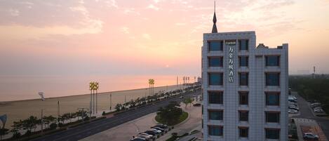 A high-rise hotel with multiple floors, a prominent spire, and a view of the beach at sunset.