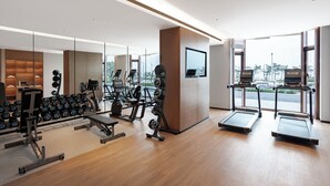 Una palestra moderna con macchinari cardio, attrezzi per pesi e uno schermo televisivo.