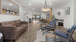 Een moderne woonkamer met een bruine leren bank, een blauwe fauteuil en een ronde salontafel. Achtergrond toont een eethoek met een houten tafel en stoelen.