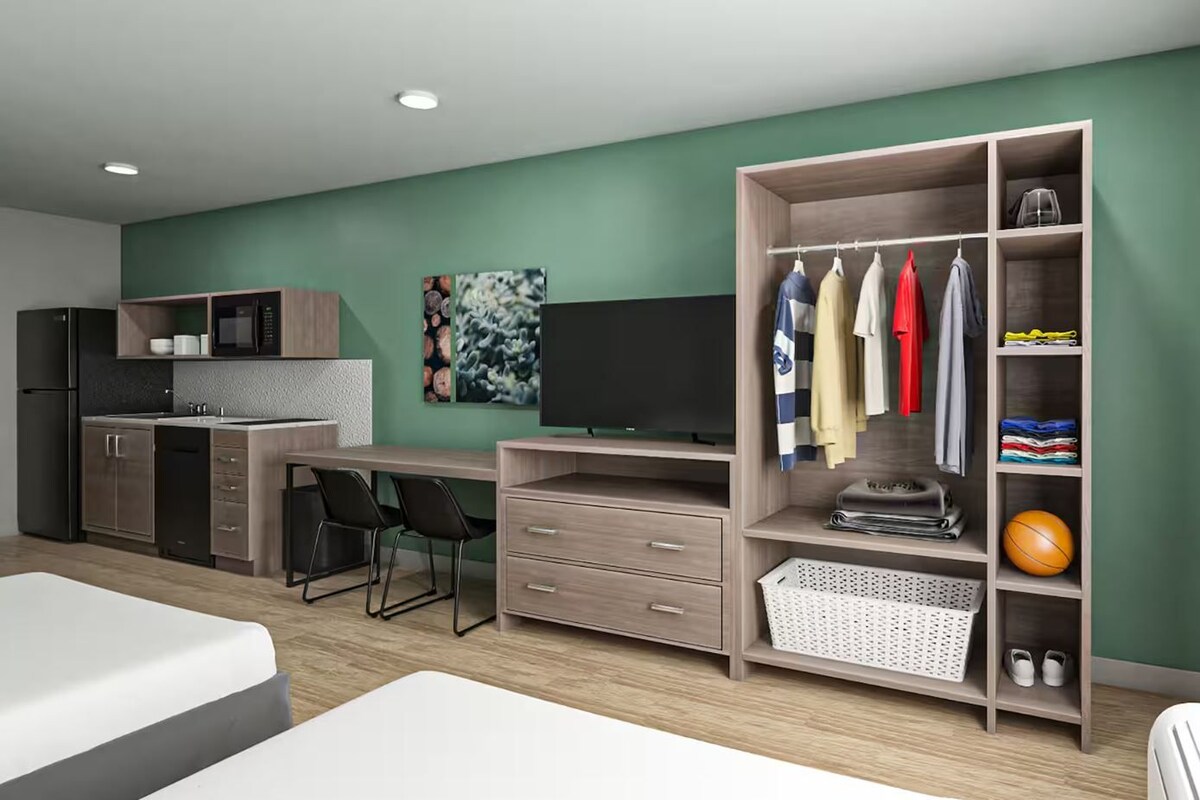 A modern bedroom with a bed, a desk, a kitchenette, and a wardrobe.