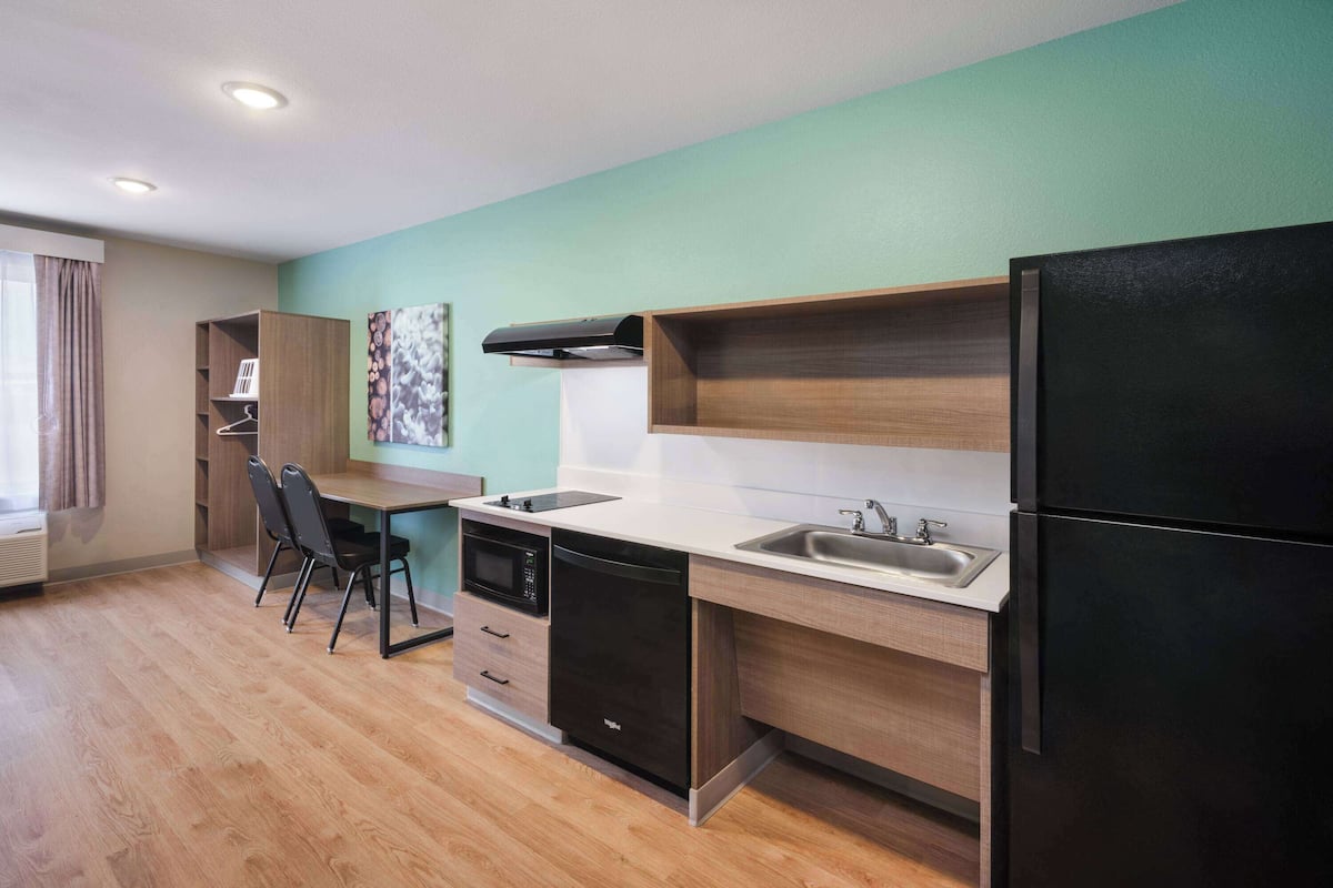A modern kitchen with a dishwasher, oven, and black refrigerator. There is a wooden dining table with chairs and a window with curtains.