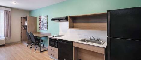 A modern kitchen with a dishwasher, oven, and black refrigerator. There is a wooden dining table with chairs and a window with curtains.