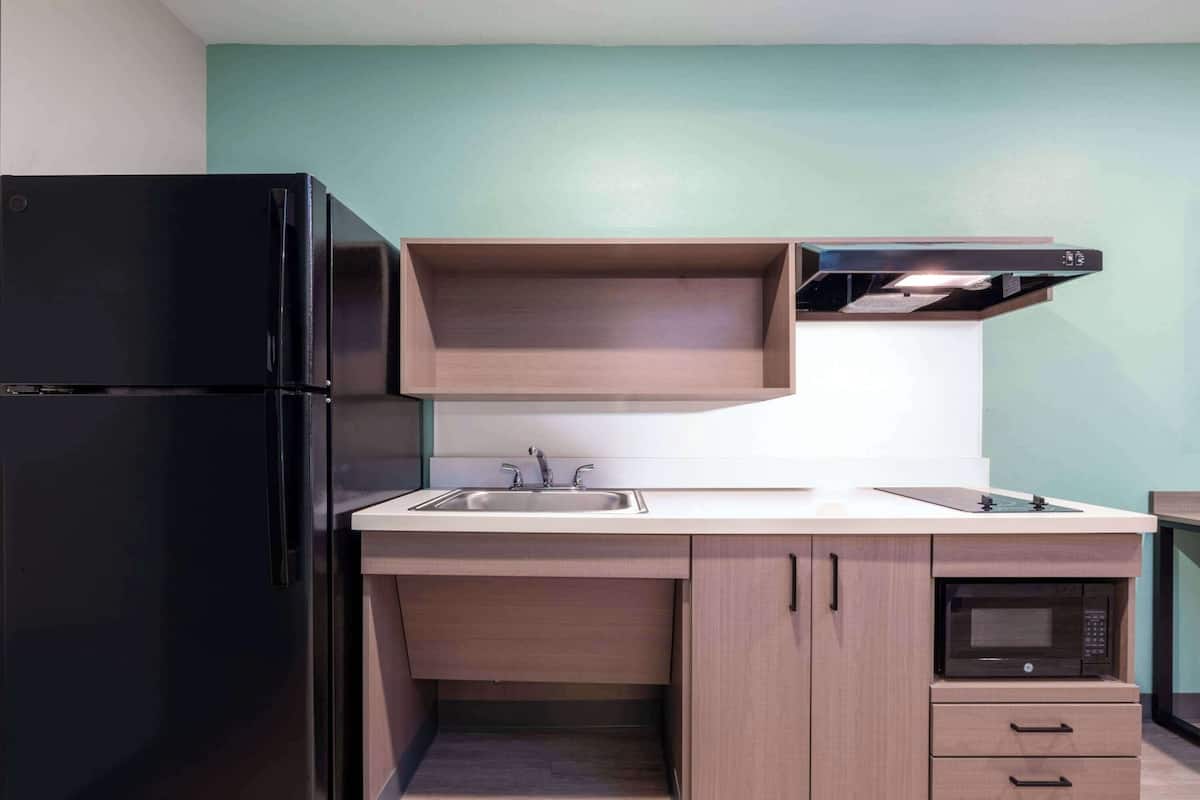 A compact kitchen with a black refrigerator, a sink, a microwave, and wooden cabinets.
