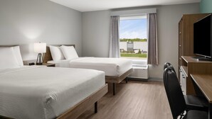Une chambre d’hôtel avec deux lits, un bureau, une chaise, une télévision et une fenêtre avec des rideaux.