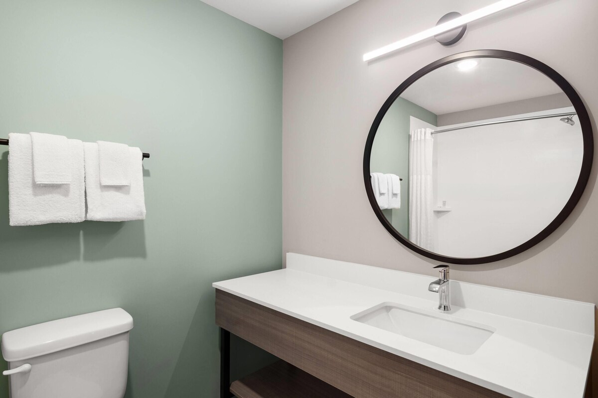 Une salle de bain avec un lavabo blanc, un miroir rond et des toilettes.