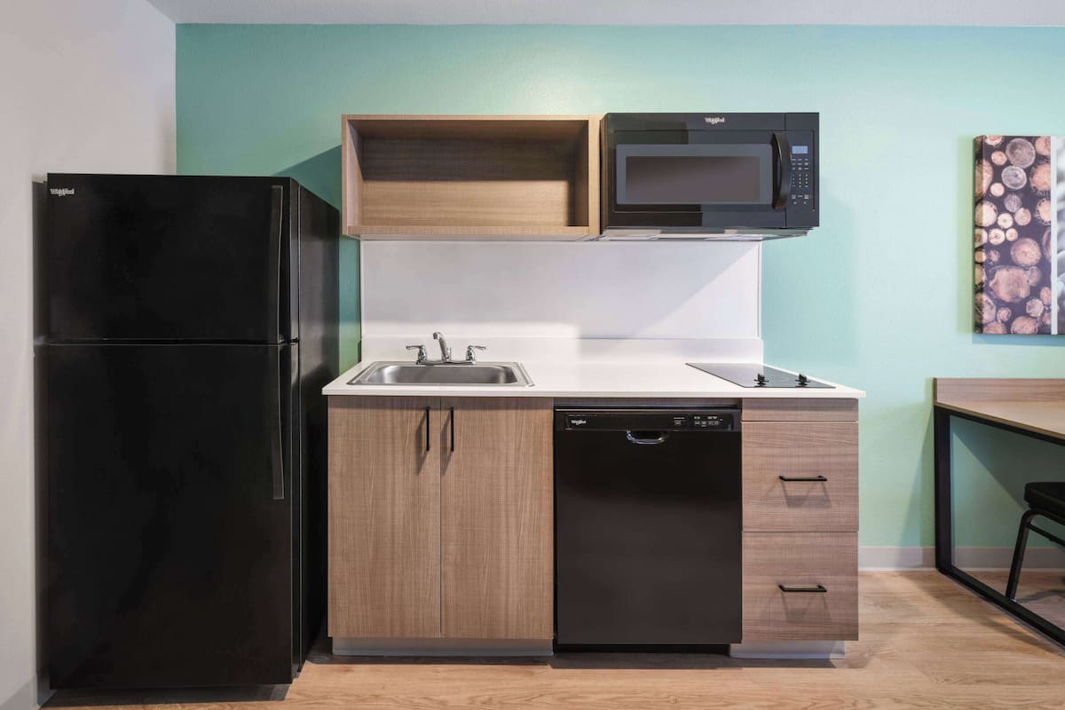 A compact kitchen with a black refrigerator, a microwave, a dishwasher, and wooden cabinets.