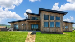 Ein modernes Holzhaus mit großem Balkon, großen Fenstern und einem Rasenstück.