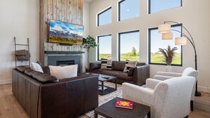 Ein modernes Wohnzimmer mit Kamin, Ledersofas, einem Couchtisch und großen Fenstern mit Blick ins Freie.