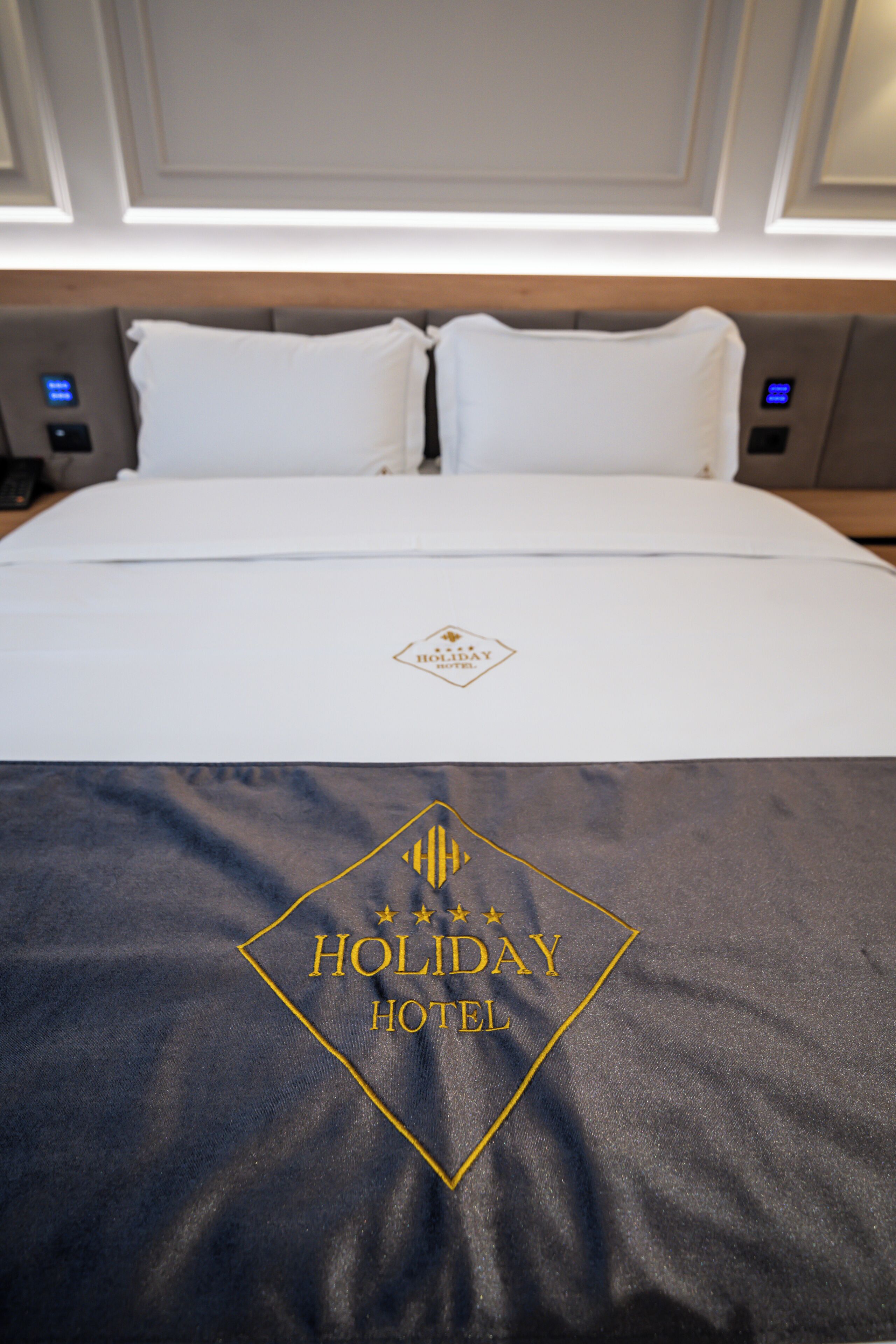 Una cama de hotel con un logotipo en la colcha y un cabecero con panel de control.