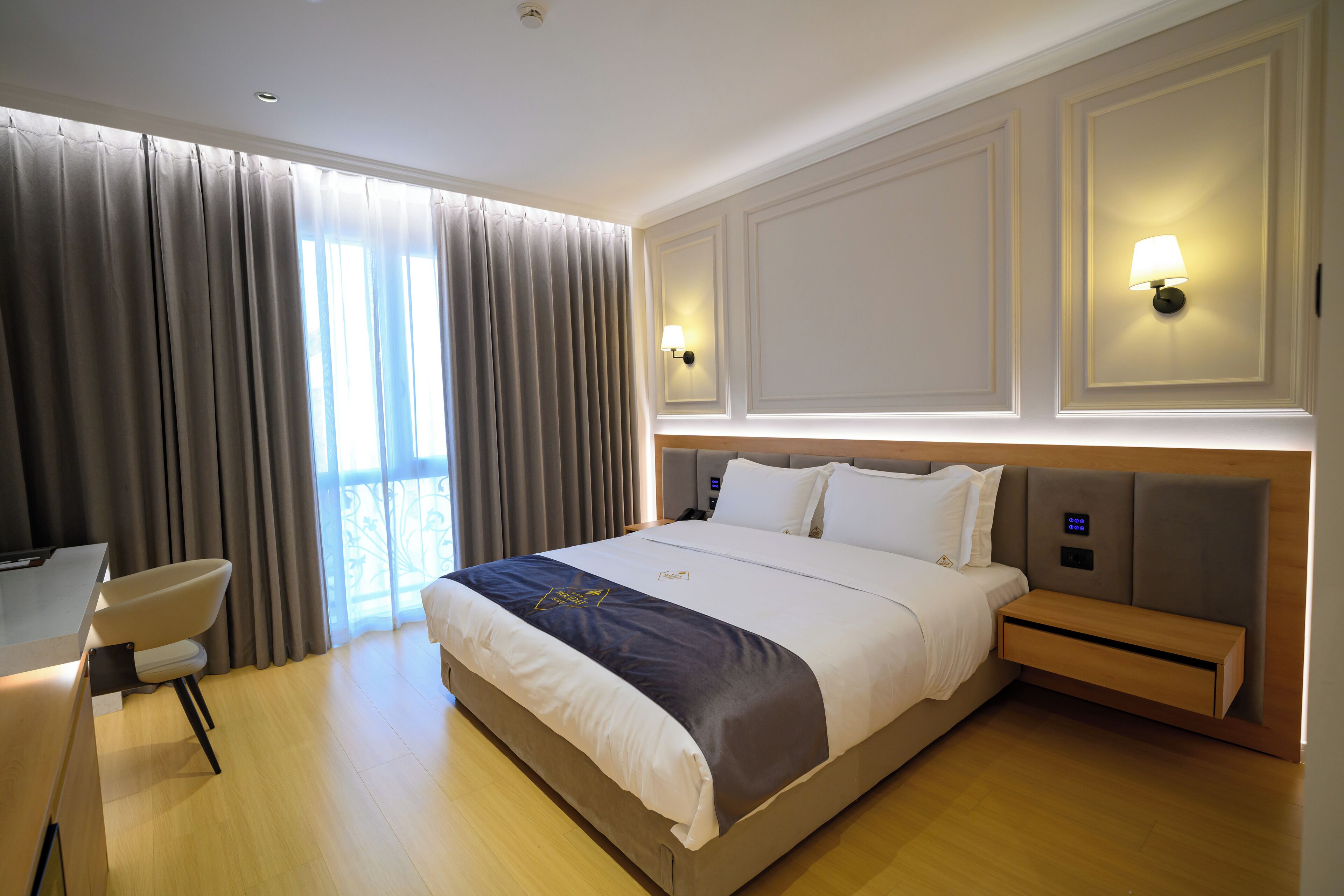 Una habitación de hotel con una cama grande, mesitas de noche, un escritorio y cortinas.
