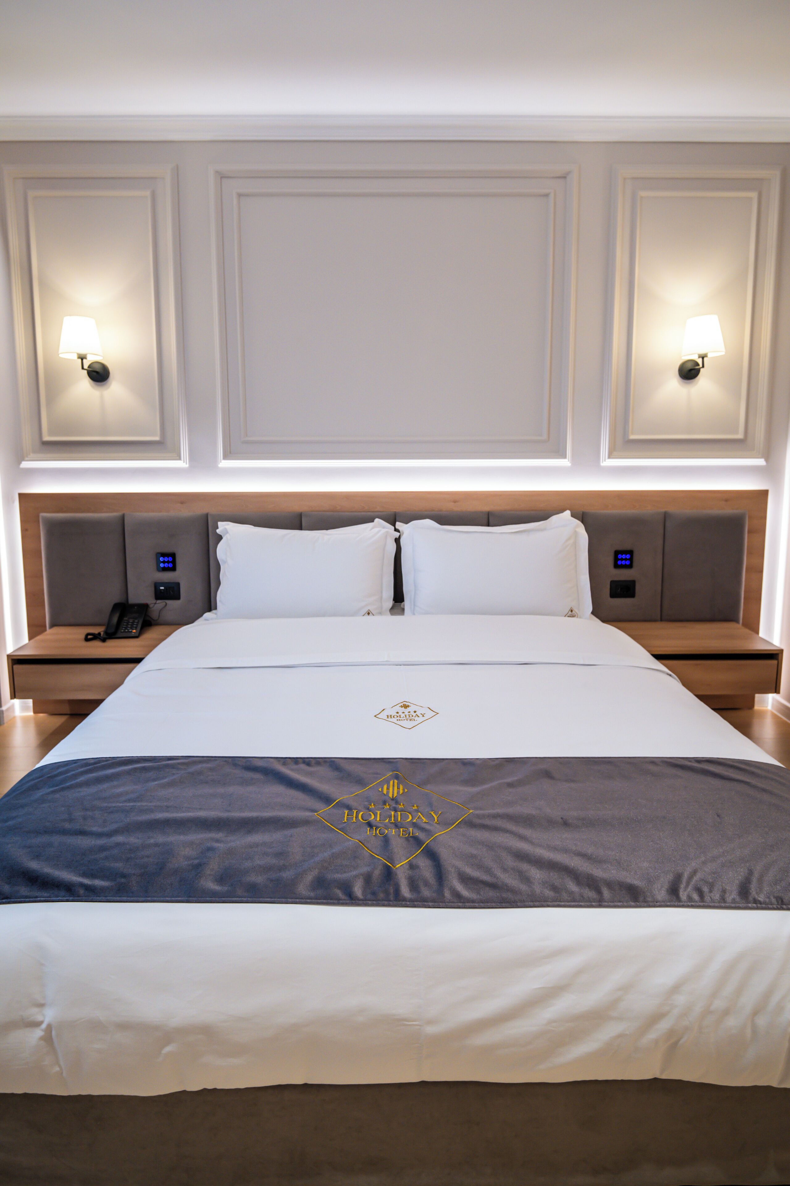 Una habitación de hotel con una cama grande, dos mesitas de noche, un teléfono y lámparas de pared.
