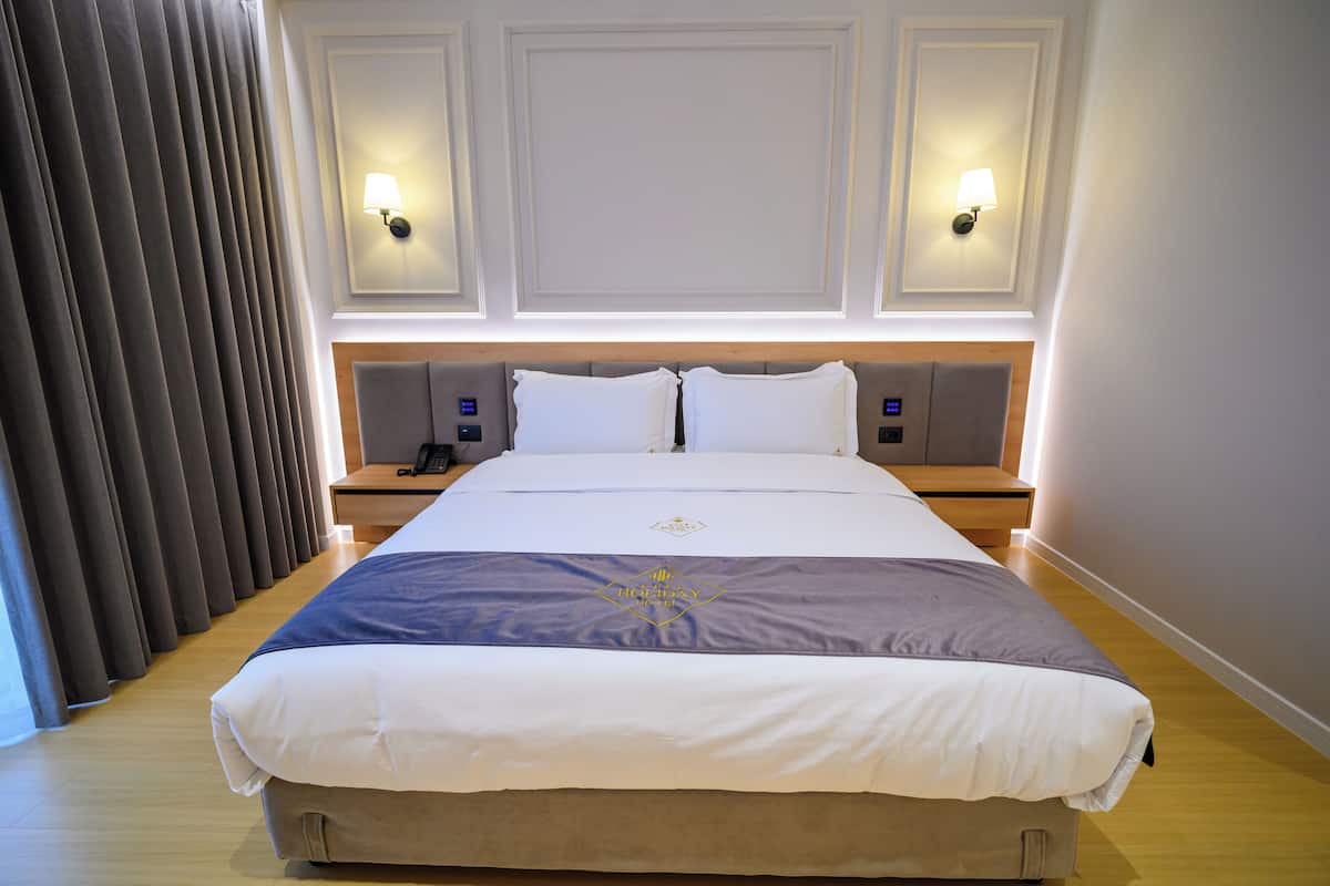 Une chambre d’hôtel avec un grand lit, deux tables de chevet, une petite table et une lampe fixée au mur.