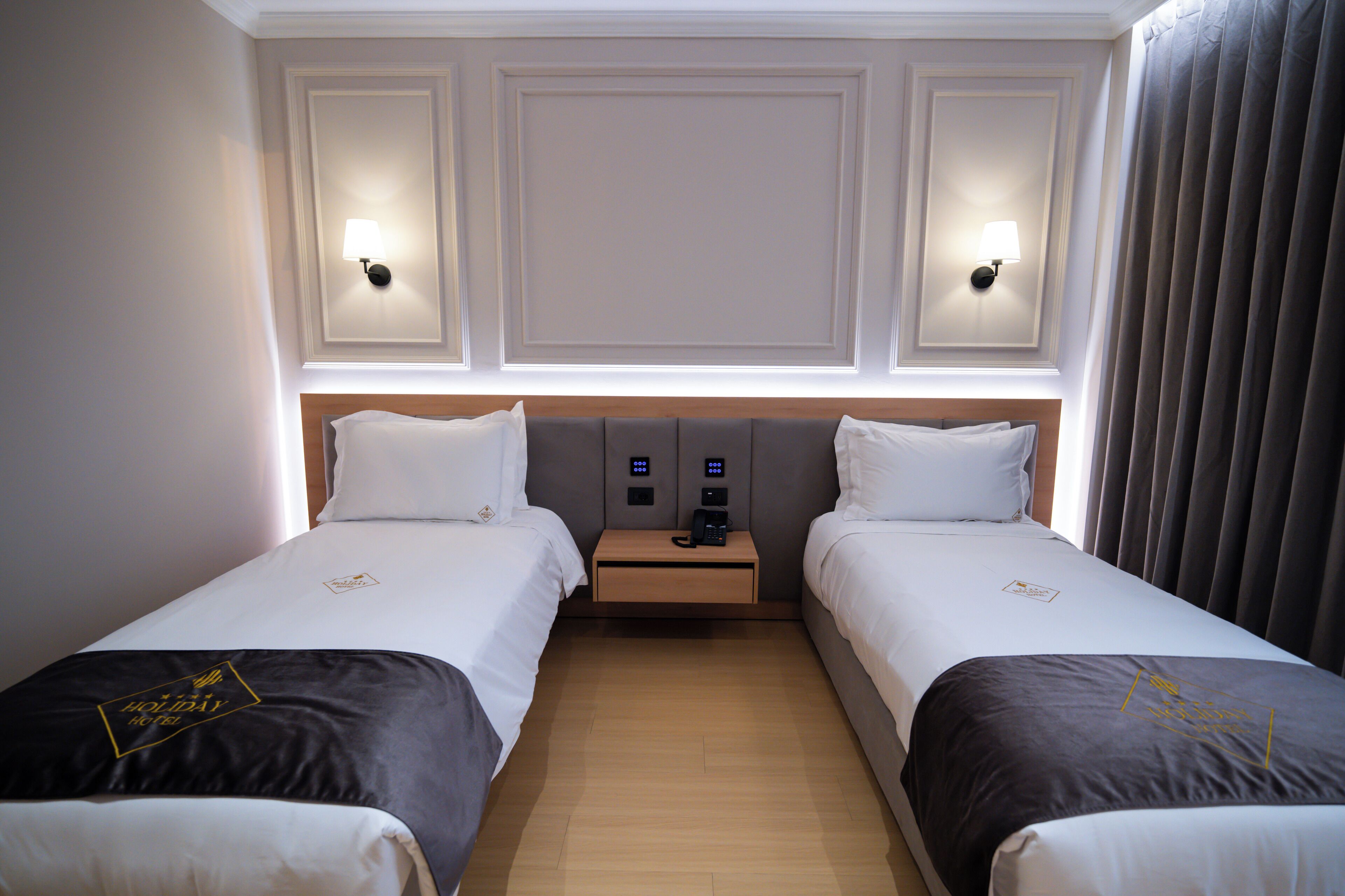 Une chambre d’hôtel avec deux lits, une table de chevet avec une machine à café et des lampes fixées au mur.